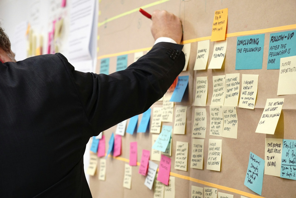 A man arranges sticky notes on a wall-mounted visual board